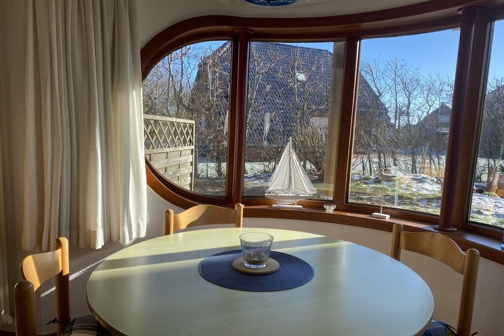 Ein Essbereich mit einem runden Tisch, Stühlen und Blick auf eine verschneite Landschaft durch große Fenster.