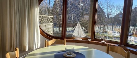 A dining area with a round table, chairs, and a view of a snowy landscape through large windows.