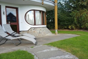 A house with a curved front, a stone base, and a paved driveway leading to a lawn. - Holiday apartment with 2 bedrooms (Friedrichskoog-Spitze)