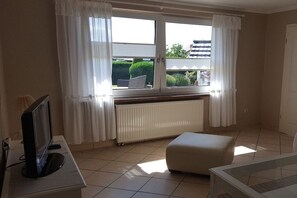 A room with a window, a radiator, a television, and a sofa. - Holiday home with 1 bedroom (Ostseebad Rerik)