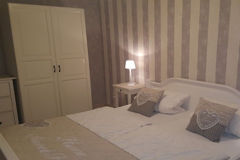 Un dormitorio con cama, almohadas, mesita de noche, lámpara y armario.
