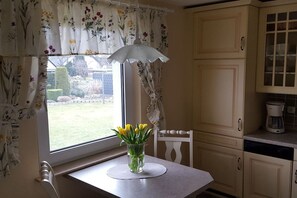 A kitchen with a window, a table with a vase of flowers, and a coffee maker. - Holiday home with 1 bedroom (Ostseebad Rerik)