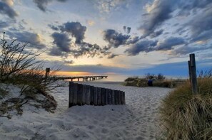 A beach with a wooden pier extending into the water, sandy dunes, and sparse vegetation. - Holiday home with 1 bedroom (Ostseebad Rerik)