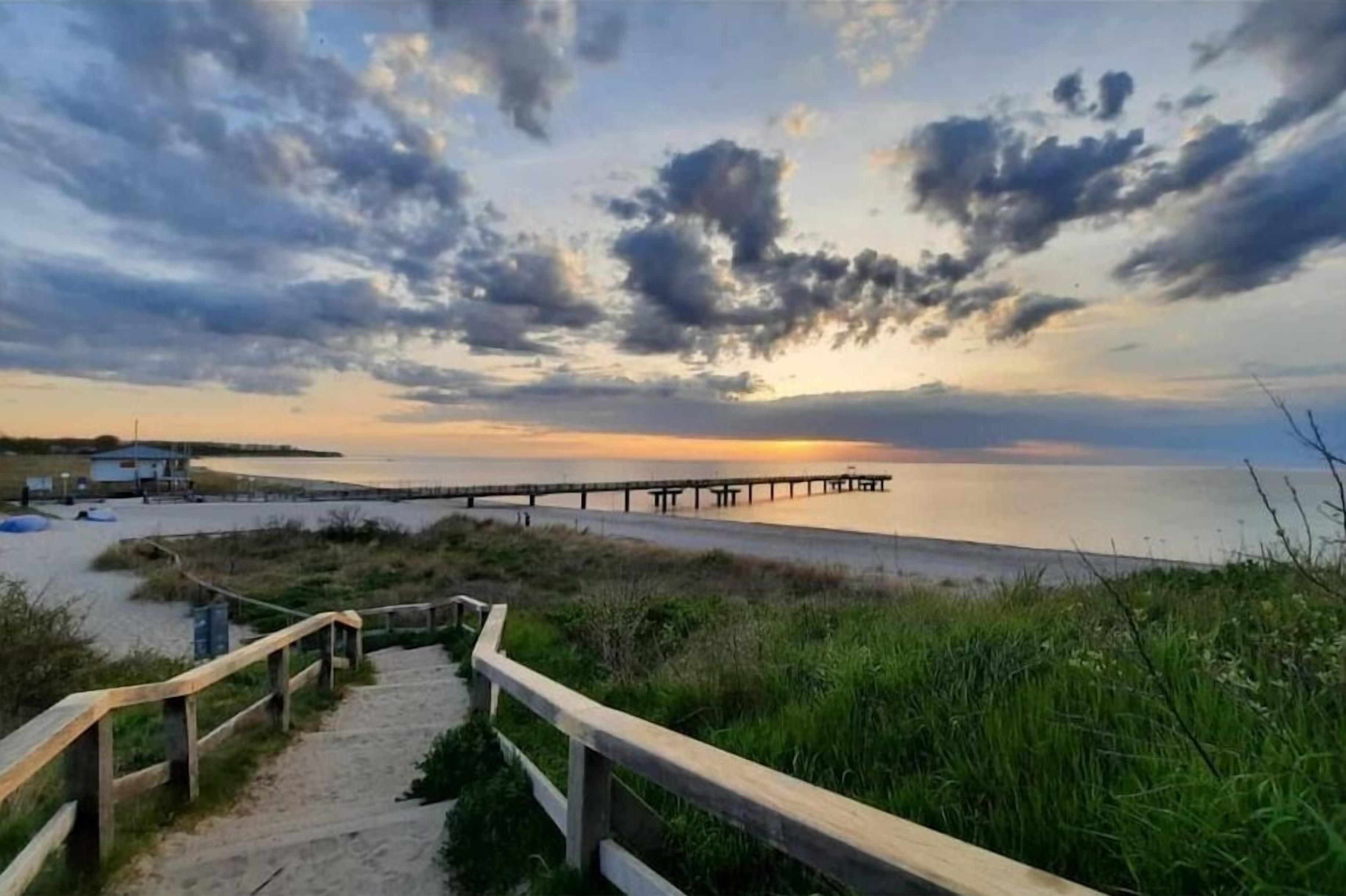 A wooden staircase leading to a beach with a pier extending into the water.