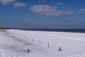 Ein schneebedeckter Strand mit einem Zaun und einer Person in der Ferne.