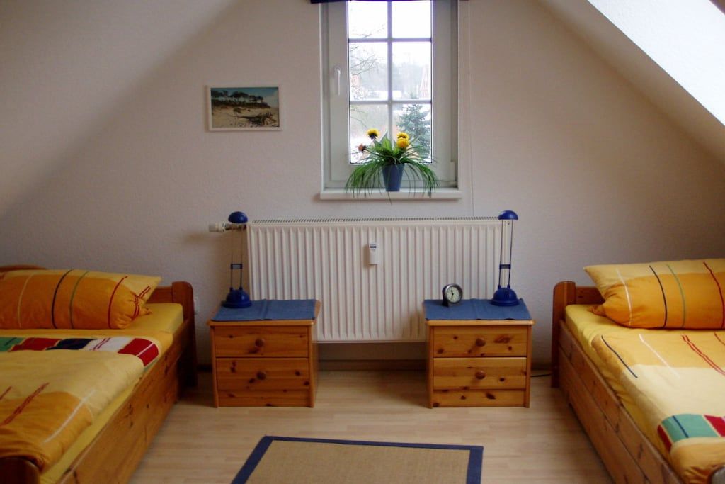 Ein Zimmer mit zwei Betten, einem Fenster mit Blick, einem Heizkörper und einem kleinen Tisch mit einer Lampe.