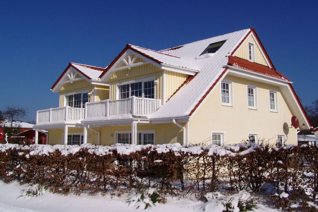 A two-story house with a balcony, a red roof, and a snow-covered ground.