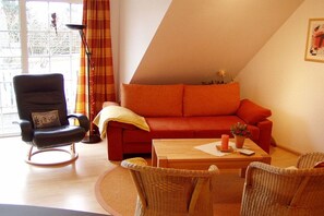 Ein Wohnzimmer mit einem roten Sofa, einem schwarzen Sessel, einem Holztisch und Korbstühlen.