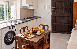 A kitchen with a washing machine, a dining table with breakfast items, and a large wooden door. - Amazing home in Adra with WiFi (Adra)