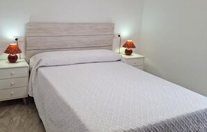 Una cama bien hecha con un cabecero de color claro y dos mesitas de noche con lámparas.