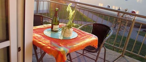 A balcony with a table set for two, a bottle of wine, and a potted plant.