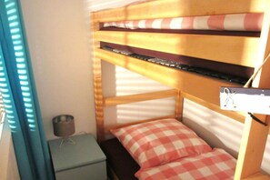 Un lit superposé avec un oreiller à carreaux, une petite table de chevet et une étagère fixée au mur.