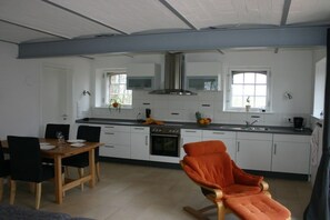 Eine moderne Küche mit weißen Schränken, eine Essecke mit Holztisch und Stühlen sowie ein Schaukelstuhl.