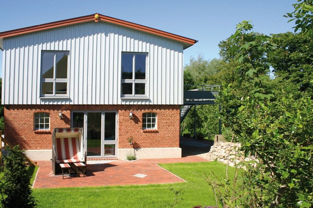 A two-story building with a brick facade and white siding, featuring a patio with a striped chair and a small table.