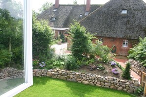Ein Haus mit einem Strohdach, einer Steinmauer und einem Garten mit verschiedenen Pflanzen und Blumen.