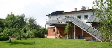 Ein zweistöckiges Gebäude mit überdachter Terrasse, einer Treppe und einem Rasen.
