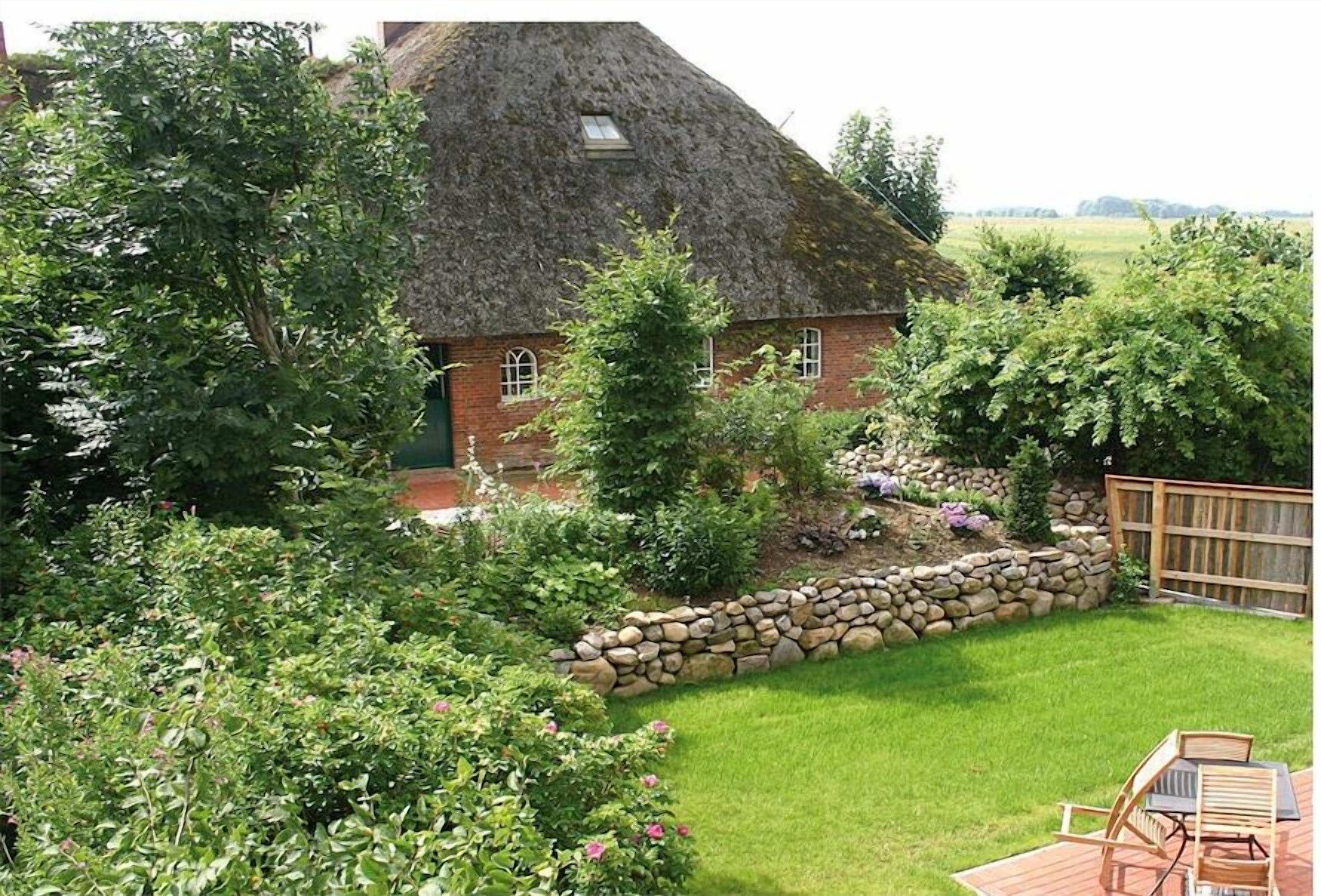 A thatched-roof house with a stone wall and a grassy yard.