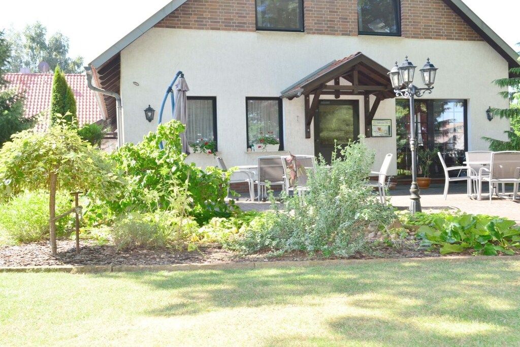 Ein Gebäude mit überdachter Terrasse, Sitzgelegenheiten im Freien und einem Garten mit verschiedenen Pflanzen.