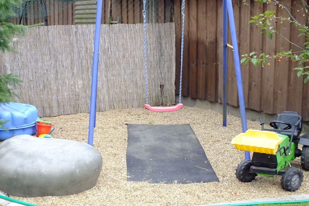 A playground with a swing set, a sandbox, and a toy tractor.