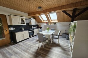 Eine moderne Küche mit Oberlichtern, Holzbalken und einem Essbereich mit weißem Tisch und Stühlen.