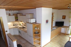 Een kleine keuken met witte kastjes, een magnetron en een spoelbak. Er is een houten aanrecht en een televisie in een hoek.