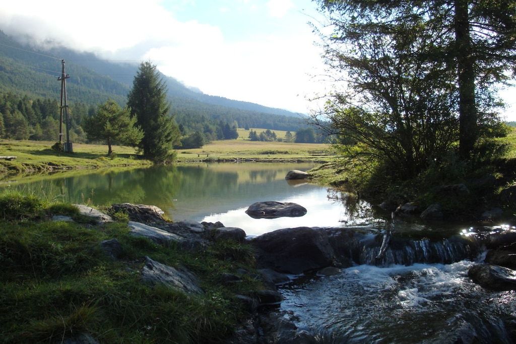 Paisagem natural com um lago tranquilo, uma cascata e uma montanha ao fundo.