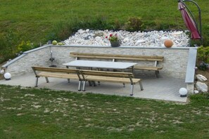 Een terras met een stenen muur, houten banken en een tafel.