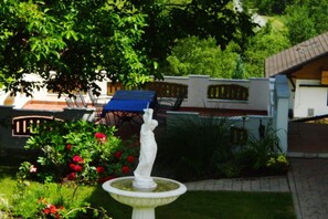 Ein Garten mit einer weißen Statue, roten Blumen und einem blauen Tisch unter einem Baum.