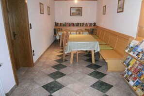 Een kamer met een eettafel, stoelen, een bankje, een boekenkast en een deur.