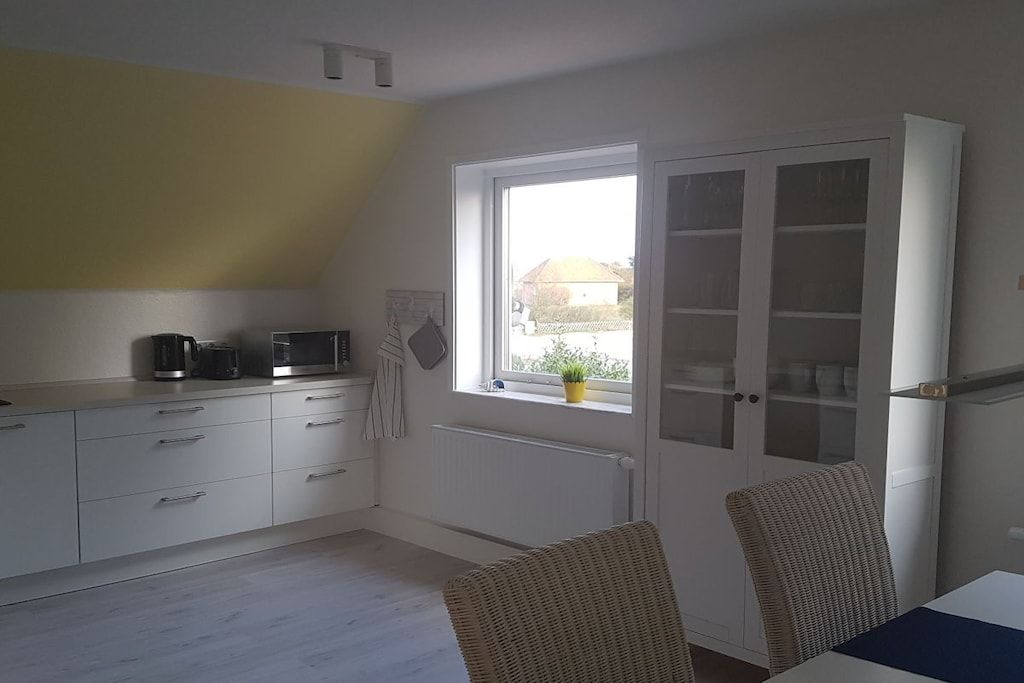 A kitchen with white cabinets, a microwave, and a coffee maker. There's a window with a view of a house and a plant on the windowsill.