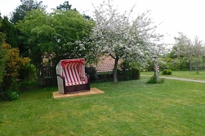 Ein Garten mit einem Sitzbereich im Freien in Rot und Weiß gestreift, umgeben von Grünpflanzen und einem blühenden Baum.