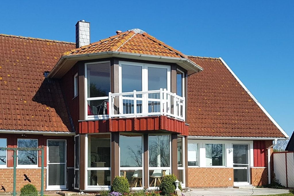 Un immeuble résidentiel de deux étages, doté d’une façade rouge, de grandes fenêtres et d’un balcon.