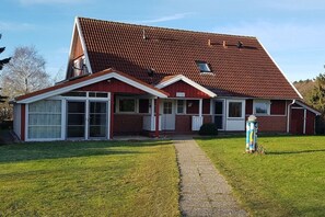 A two-story house with a sloped roof, a front porch, and a pathway leading to the entrance. - Holiday apartment with 1 bedroom (Hohwacht)