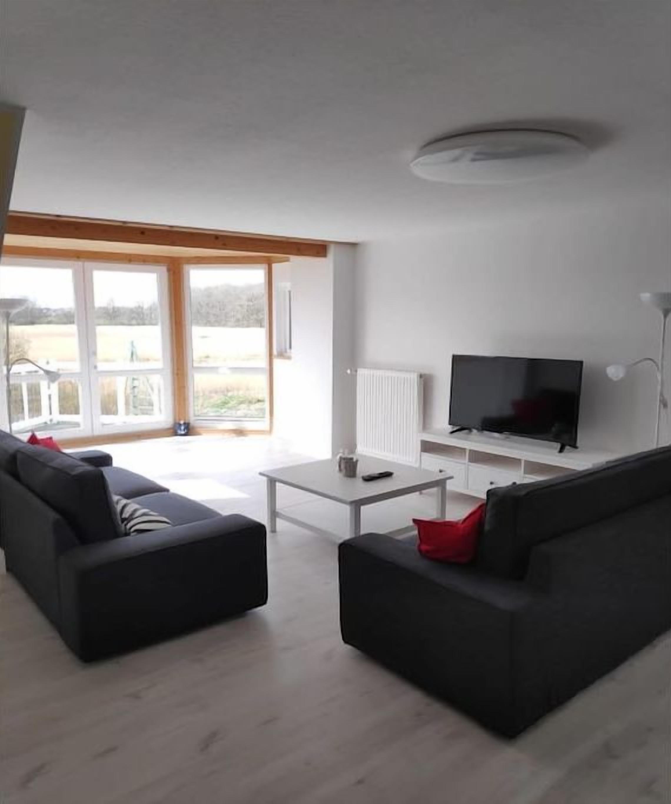 Een moderne woonkamer met een flatscreen televisie, twee banken, een salontafel en een glazen schuifdeur die leidt naar een balkon.