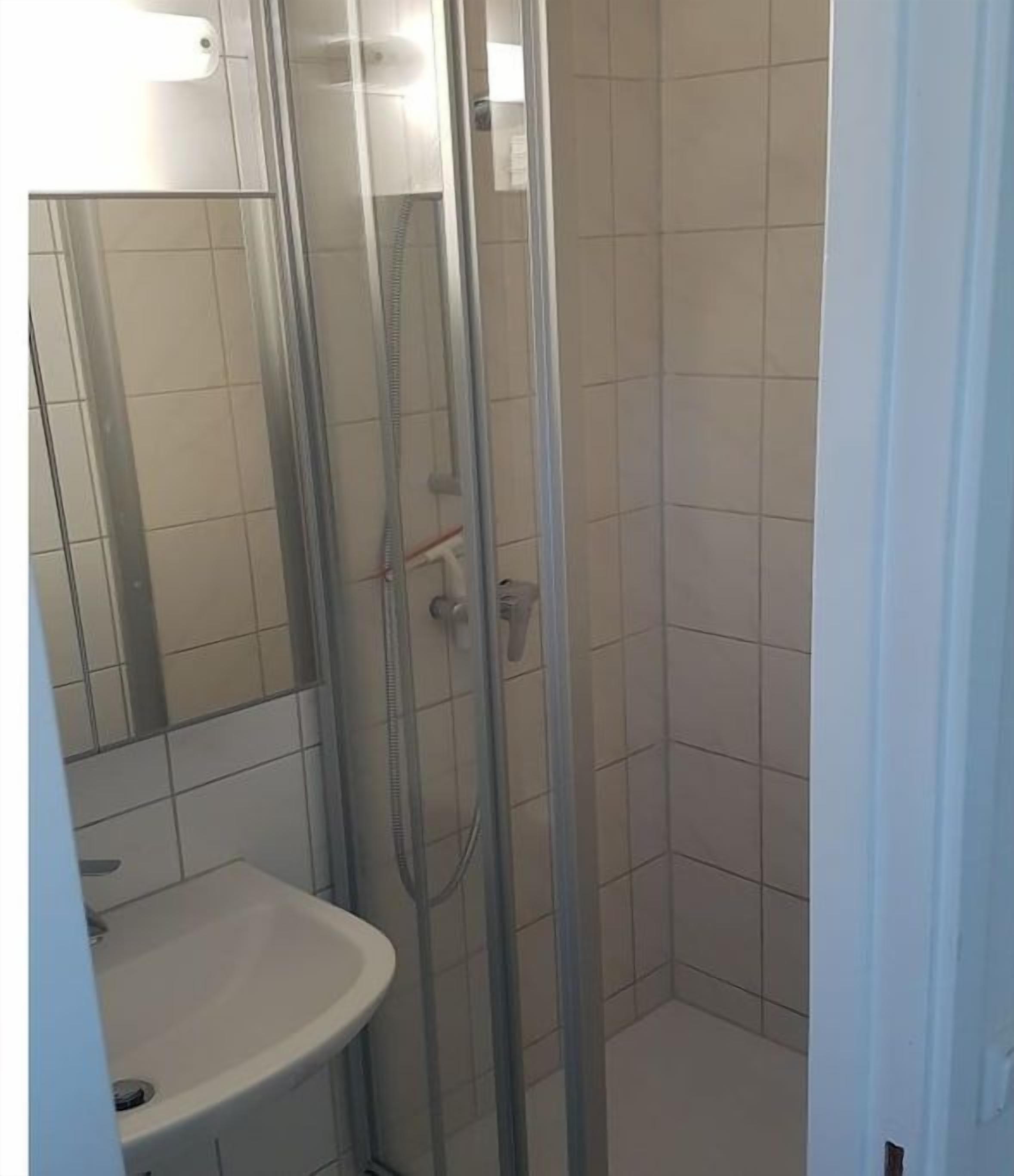Un bagno con doccia vetro, lavandino bianco e pareti piastrellate.