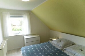 Ein Schlafzimmer mit Bett, Nachttisch, Kommode und einem Fenster mit Vorhängen.