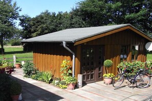 Eine Holzhütte mit geneigtem Dach, einer Tür und Fenstern. Vor der Hütte steht ein Fahrrad.