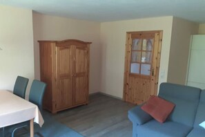 Ein Zimmer mit Esstisch, zwei Stühlen, einem blauen Sofa, einem Holzschrank und einer Tür mit Fenster.