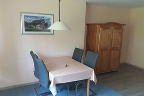 Ein Essbereich mit Tisch und Stühlen, einer Hängelampe, einem Holzschrank und einem gerahmten Bild an der Wand.