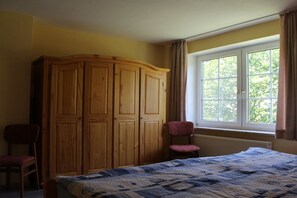 Ein Schlafzimmer mit einem Bett, einem Holzschrank, einem Stuhl und einem Fenster mit Vorhängen.