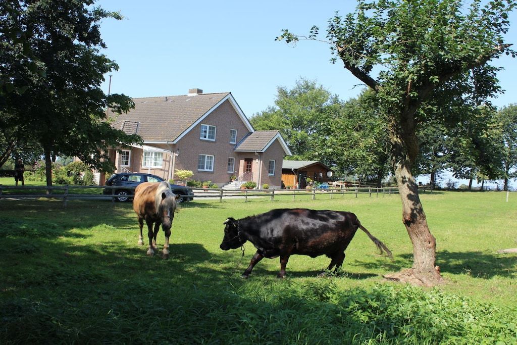 Ländliche Landschaft mit einem Haus, einer Kuh und einem Pferd auf einer Wiese.