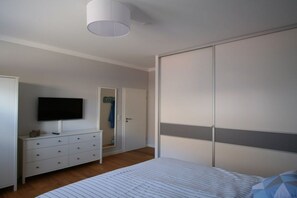 A bedroom with a bed, a television on a dresser, a wardrobe, and a door leading to another room. - Holiday apartment with 1 bedroom (Orth\/ Fehmarn)
