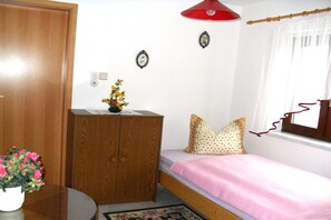 Een slaapkamer met een houten garderobe, een bed met een roze dekbedovertrek, een rode hanglamp en een raam met witte gordijnen.