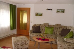 Een woonkamer met een bank, een poef en een kleine tafel met een vaas.