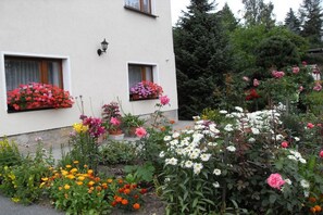 Ein Gebäude mit zwei Fenstern, jedes mit einem Blumenkasten voller roter und pinker Blumen.