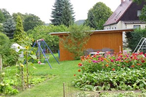 Een woon tuin met een schommel, een houten tuinhuis en diverse bloeiende planten.