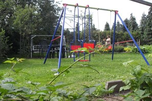 Ein Spielplatz mit Schaukeln und einer Rutsche, umgeben von Grünflächen und einem Garten.