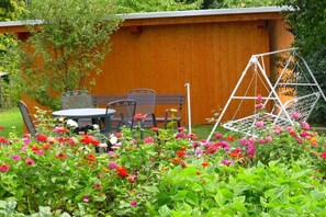 Um jardim com um galpão de madeira, uma mesa com cadeiras e uma estrutura de escalada branca.