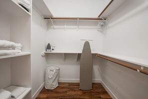 A compact, white-walled closet with wooden flooring, featuring shelves, a hanging rack, and a neatly folded stack of towels. - Heated Pool & Outdoor Theater, Close to DT, UT (Austin)