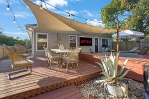 A deck with outdoor furniture, a table, and chairs, a pool, and a Netflix sign. - Heated Pool & Outdoor Theater, Close to DT, UT (Austin)